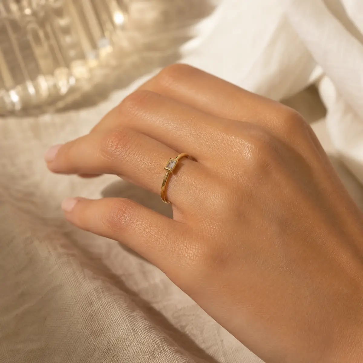 Gold ring on a woman's hand in warm editorial light, soft beige linen background